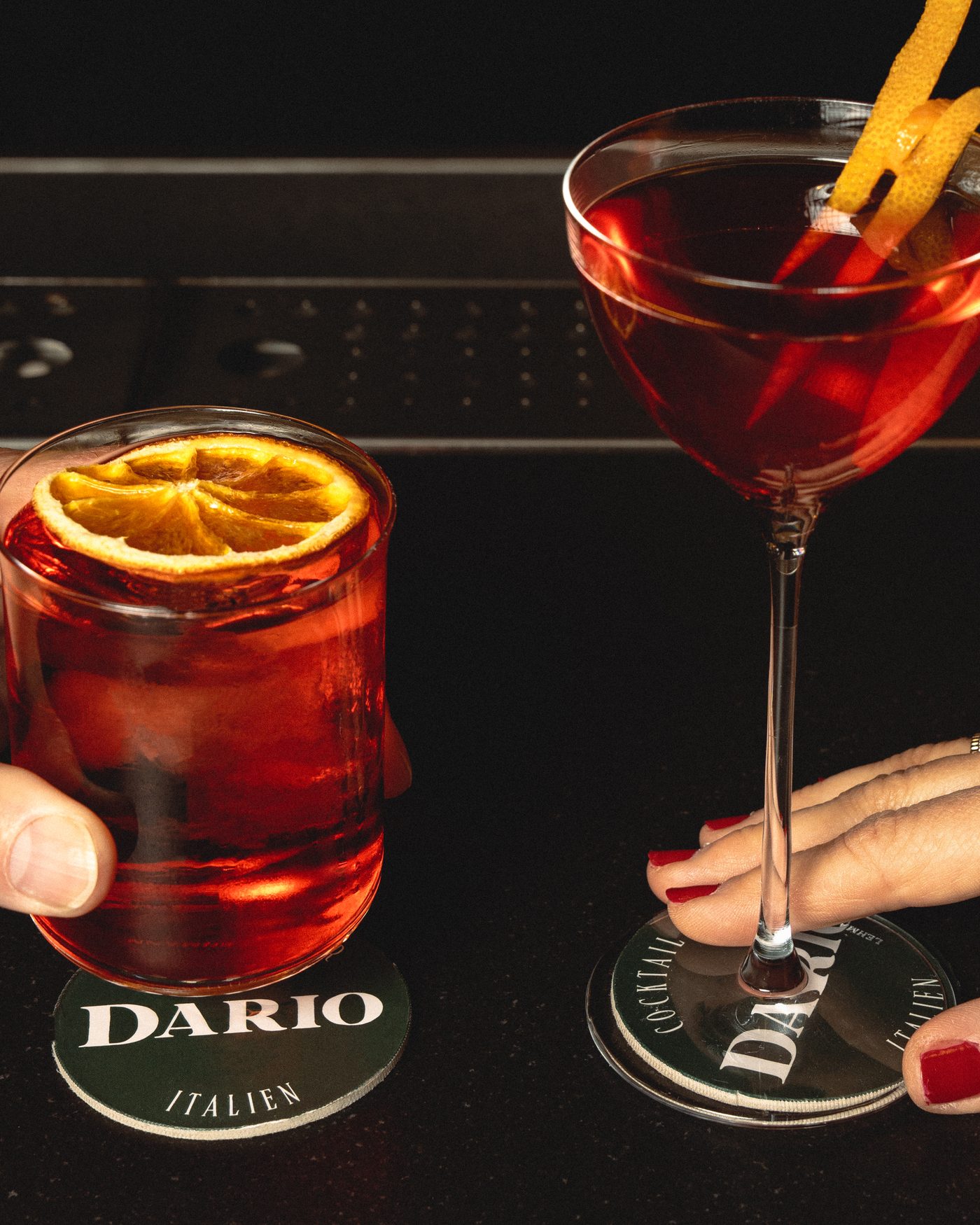 Deux cocktails trinquent sur les sous-verres Dario, dans la pénombre du bar